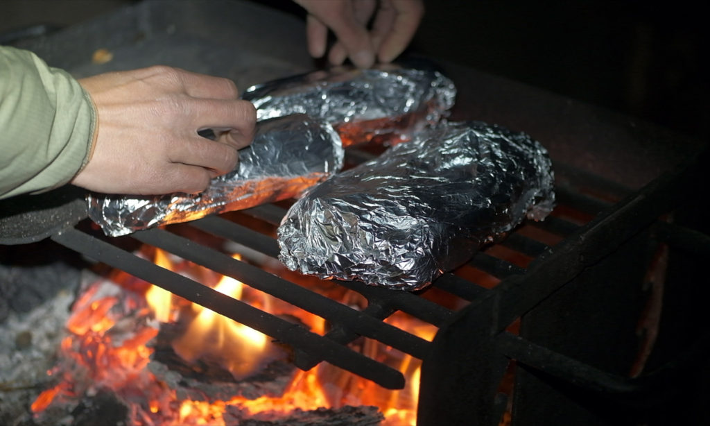 Cooking chicken wings in tin foil over a camp fire grill