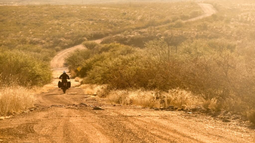 Lone motorcyclists riding into sunset on a dirt road