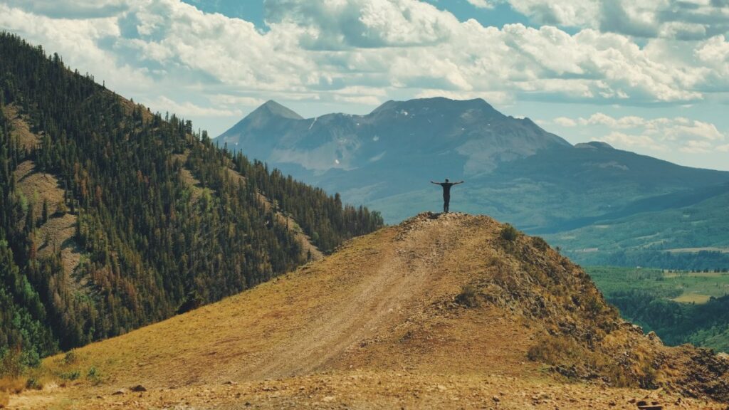 Man standing with arms outstretched on hill top