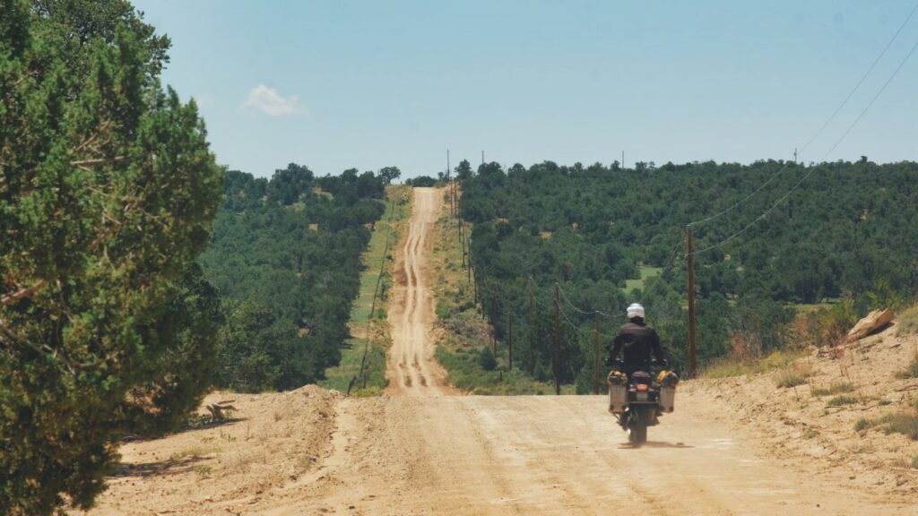 Sterling Noren riding motorcycle on long dirt road in New Mexico