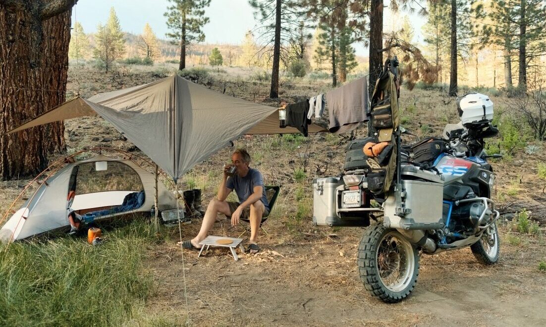 Sterling Noren with BMW motorcycle camping under a tarp